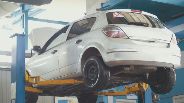 Car in auto service lifting for repairing, mechanics in garage, close up