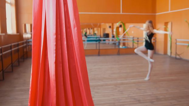 Red silk in front of young woman training a gymnastics exercise with a ribbon, blurred