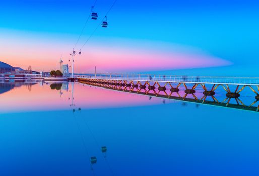 Picturesque sunset over The Park of the Nations in Lisbon, Portugal. Evening cityscape with cable car road and bridge reflected in the water