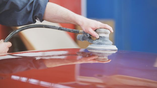 Professional car service - a worker polishes a red automobile, telephoto
