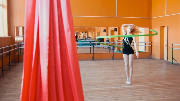 Rhythmic gymnastics - young woman training a gymnastics exercise with a green ribbon, wide angle