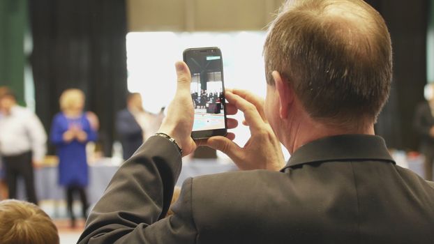 Bald man shooting a smartphone award at the tournament, rear view, close up