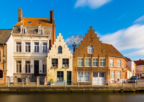 Bruges (Brugge), Belgium: Street view of the old residential houses in traditional architecture style. Facades of the historical buildings and canal with water.