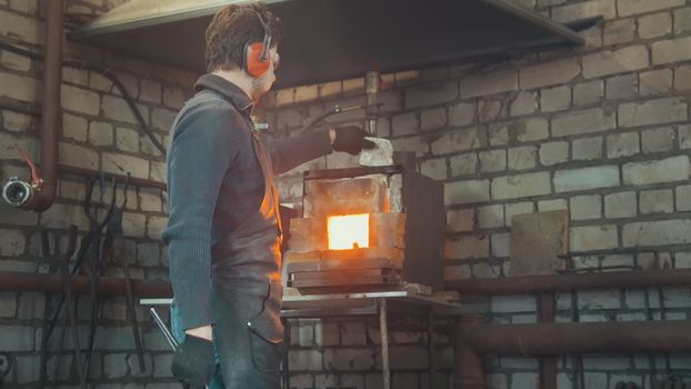 Blacksmith with gloves in forge makes steel knife, small business