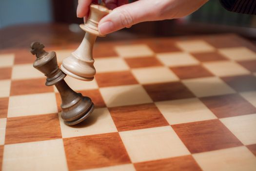 Concept: the woman who dominates the man. A woman's hand gives checkmate to the king with the queen on a wooden chessboard, with no other pieces in play