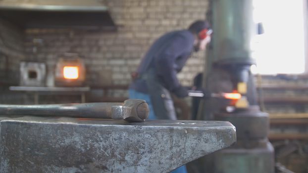Molten metal is processed under pressure in the hands of a blacksmith, in the forge, wide angle shot
