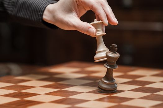 Concept: the woman who dominates the man. A woman's hand gives checkmate to the king with the queen on a wooden chessboard, with no other pieces in play