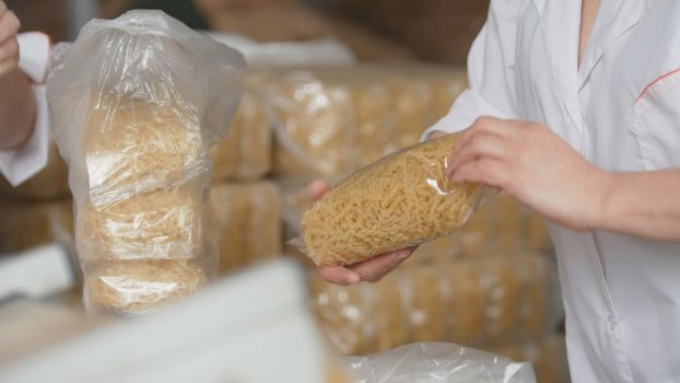 Workers packaging raw macaroni from the production line in a pasta manufactury, telephoto shot