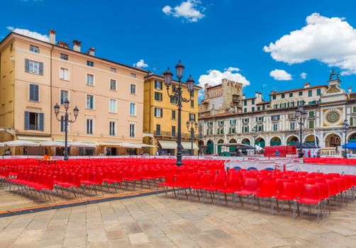 Brescia - July 2017, Italy: The central square of Brescia (Piazza della Loggia) with old architecture, street lamps and empty, plastic red seats prepared for a concert