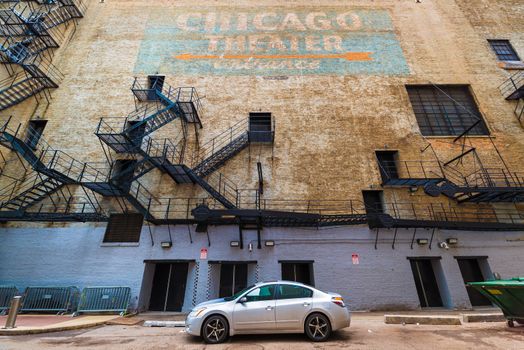Chicago - March 2017, Illinois, USA: Wide angle view of Chicago Theater wall with fire stairs, doors, hand written graffiti sign with orange arrow on blue background, car parked on the street