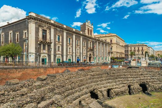 Catania - April 2019, Sicily, Italy: Roman Amphitheater of Catania, ruins of an ancient theater. View of Palace of Tezzano (Palazzo Tezzano) on Stesicoro Square