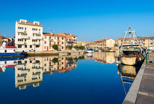 Grado - December 2015, Italy: Colored houses and boats with their reflections in water of one of the canals of Grado