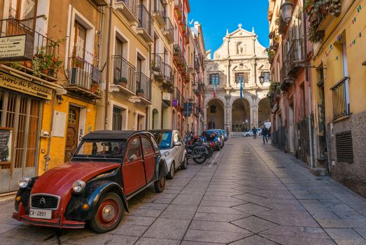 Cagliari - January 2 of 2016, Sardinia, Italy: Street view with old houses, Church and Vestry of Saint Michele and vintage red car on Via Domenico Alberto Azuni
