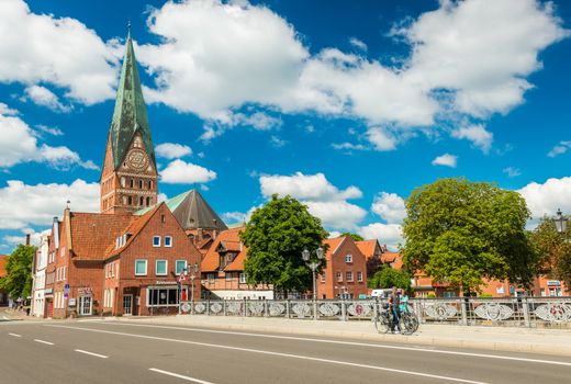 Luneburg - July 2018, Lower Saxony, Germany: People walking along the bridge. Cathedral and old historical houses with blue sky and clouds on the background