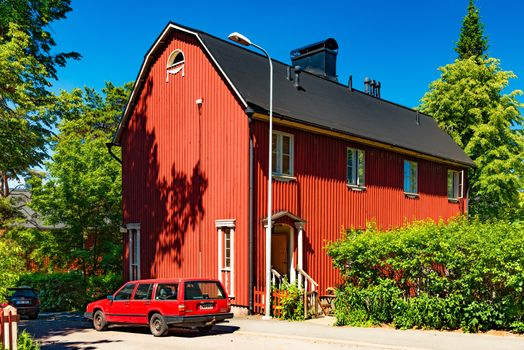 Helsinki - June 2019, Finland: Red wooden residential house on one of the streets in neighbourhood Helsinki. A red car parked near an old house