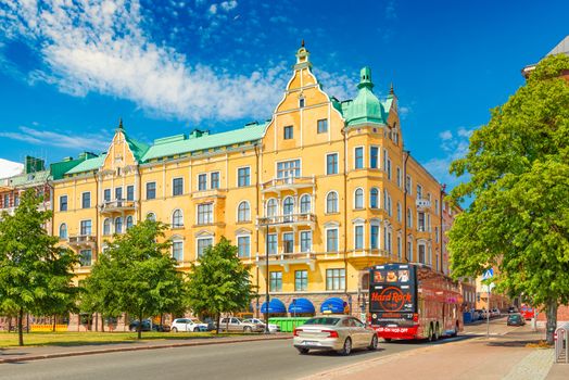 Helsinki -  June 2019, Finland: A street in Helsinki with car traffic and an old yellow house in the traditional architecture style