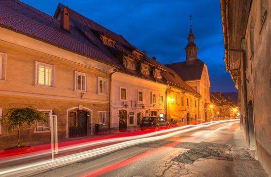 Skofja Loka - April 2015, Slovenia: Narrow street with car light trails, historical residential houses and old Church in small Slovenian town of Skofja Loka