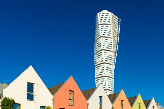 Malmo - October 2018, Sweden: View of The Turning Torso skyscraper with blue sky on the background and a row of colored residential houses in front