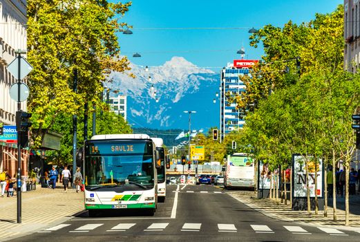 Ljubljana - September 2019, Slovenia: View of a street with public transport, crosswalk, modern architecture and the snowy Alps in the background