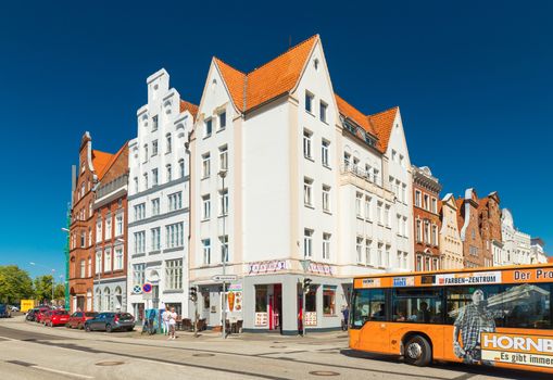 Lubeck - July 2018, Germany: Historical buildings near the embankment of Lubeck. Traditional architecture style, white and red brick houses with orange roofs. Bus is driving along the street