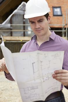 Architect On Building Site Looking At House Plans