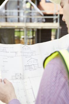 Architect On Building Site Looking At Plans For House