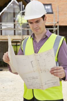 Architect On Building Site Looking At Plans For House