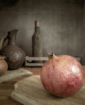 On the kitchen table on the cutting Board is a large ripe pomegranate fruit. Next to it is a kitchen knife. A dark background and copy space.