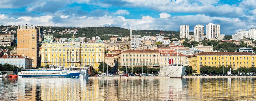 Rijeka - June of 2012, Croatia: Rijeka cityscape reflected in the water, Jadrolinija building and ships in harbour, old and modern buildings against the green hills and cloudy sky