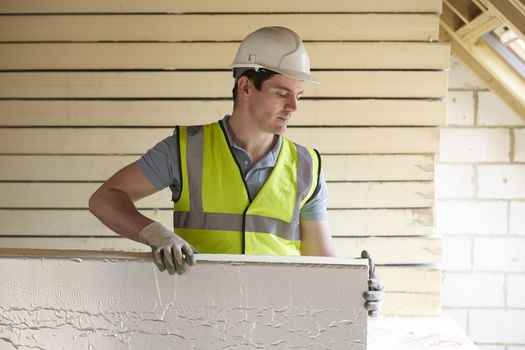 Builder Fitting Insulation Boards Into Roof Of New Home