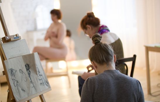 Young female artists sketching a nude model in drawing class, telephoto shot