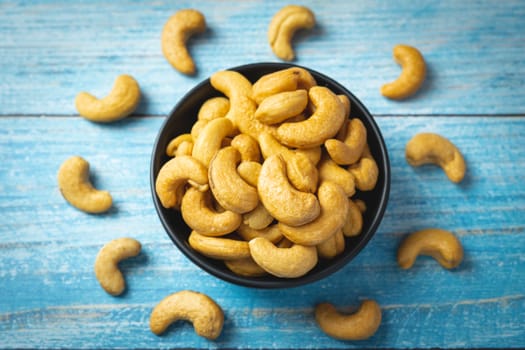 Top view of roasted cashew nut in salt in black bowl  on soft blue vintage wood table