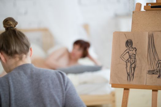 Rear view of female painter draws sketches of nude woman in drawing class, telephoto shot