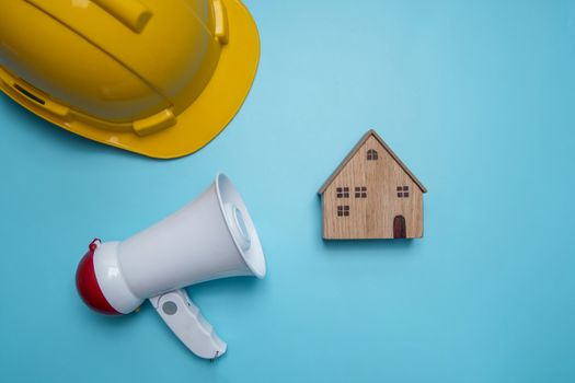 Announcement and announce advertising background public relations about construction building, home, house and real estate with megaphone and yellow helmet on blue background 