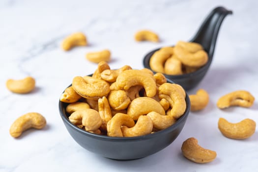 Roasted cashew nut in salt in black spoon on soft white table