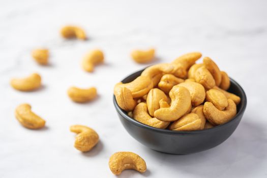 Top view of roasted cashew nut in salt in black bowl on soft white table