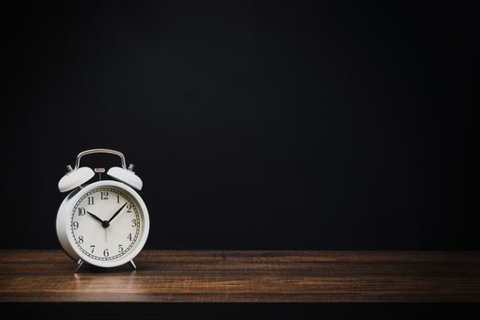 white alarm clock on wood table at night with dark or black background 