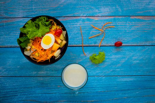 Good health and vegetarian concept, healthy vegetable salad of green fresh vegetable, carrot, corn, and fruit with milk and egg on plate on dark blue wood table background