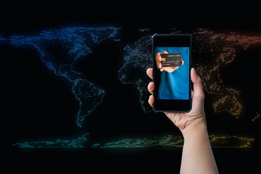 Shopping online concept. Hand holding credit card on the screen of a smartphone or mobile on the colorful world map with a black background.