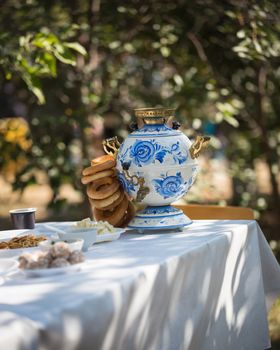 On the table with a white tablecloth is a beautiful samovar with bagels, next to other food, close up