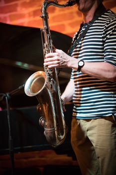 An anonymous musician in a striped t-shirt plays the saxophone in a jazz bar, live performance, close up