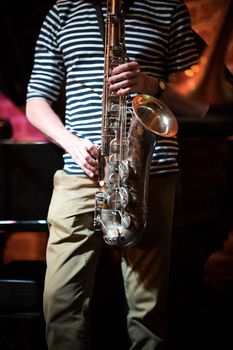 Anonymous musician in a striped t-shirt playing the saxophone at a party in a jazz bar, close up