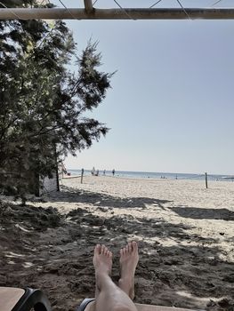 A woman is resting on a chaise longue on a sandy beach near the sea.