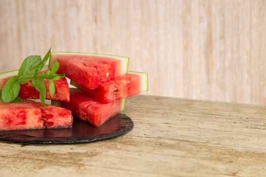 Triangular slices of watermelon overlaid on a black plate of wet slate with sprig of fresh green mint in selective focus for copy space