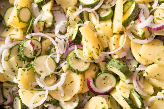 Vegan food: close-up of pan of raw vegetables sliced ​​like ratatouille with courgette, potatoes, onions and seasoned with sage, oregano and rosemary before being cooked