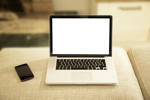 Open aluminum laptop with blank screen for copy space and smartphone on a sofa ottoman in selective focus with shaded lounge background