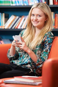 Female Teenage Student Using Mobile Phone In Library