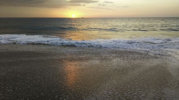 Sunset over the ocean from the shore of Nazaré beach, Playa do Norte, Portugal. The waves break on the shore reflecting the colors of the sky on the wet sand