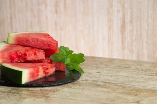 Triangular slices of watermelon overlaid on a black plate of wet slate with sprig of fresh green mint in selective focus for copy space