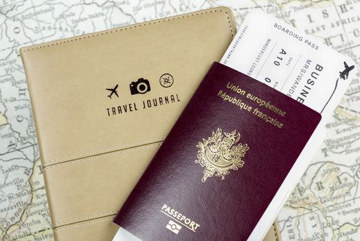 Close-up of a Travel Journal cover with 3 small logos (a plane, a camera and a compass), a passport and a boarding pass and a ancient map at background.